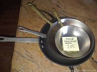 Two Calphalon Commercial line frying pans stacked inside each other, showing metal handles and interior surfaces.