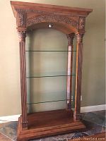 Photo shows the wooden etagere with detailed carved columns, ornate top arch, two glass shelves, and light fixture above the shelves.