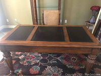 Front view of wooden desk showing three leather inset panels on the top surface and carved wooden legs.