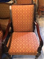 Close-up front view of one mahogany side chair showing upholstery pattern and wooden armrests