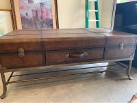 Photo showing the full trunk style coffee table with iron base, curved legs, wooden textured top and sides with metal handle and latches.