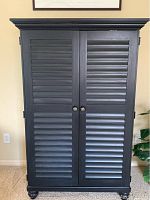 Closed view of tall black storage cabinet with shutter-style doors and round knobs