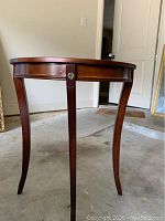 Half moon style wooden hall table by Bombay Company in a garage setting