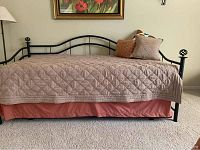 Black metal daybed with pink bed skirt, decorative finials, and pillows showing overall condition and style