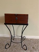 Full front view of a wooden box hall table on a black iron base stand with curled leg design on carpeted floor against blank wall.