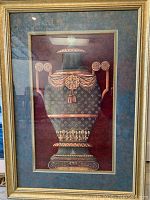 Photo of framed print showing ornate green vase with gold details on red background, in gold frame with blue matting.