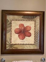 Framed 25 inch square wall art featuring a red hibiscus flower in the center with botanical leaves in the background.