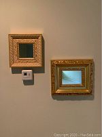 Photo of two gold-framed square decorative wall mirrors hanging on a wall. The larger mirror is 12x14 inches, and the smaller is 10x10 inches. Both have ornate gold frames with intricate details.