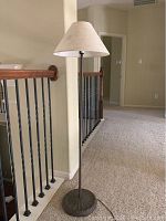 Side view of the full floor lamp showing rusted metal base, slim pole and beige fabric lampshade in hallway setting.