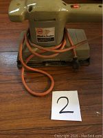 Side view of Black & Decker dual action sander showing the body and power cord wrapped around the base on wooden surface.