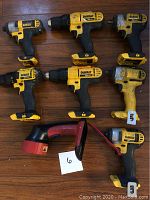 Overhead view of seven DeWalt cordless drills/drivers and one flashlight on wood floor