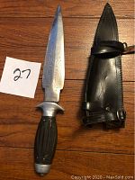 Photo showing full dagger with etched blade and dark handle beside the black leather sheath with straps.