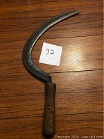 Full view of the curved sickle blade with wooden handle, placed on wooden surface with number 32 card.