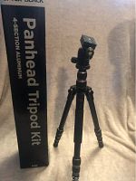 Full view of Optex Black Panhead Tripod assembled next to its box showing four-section aluminum legs and panhead setup.