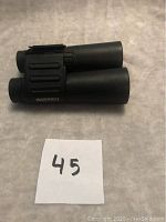 Top side view of black Bushnell binoculars showing textured grip and Bushnell branding, placed on white surface with number 45.