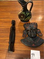 Three items on wooden floor: Mexican ceramic vase, painted mask, and dark wood Inuit figure