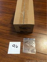 Photo of closed cardboard box containing the Ronco Zip bags with a single sample 3x3 inch bag beside it and a note with the number 96.