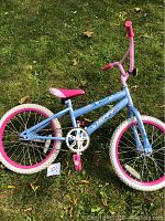 Full view of blue and pink girls bicycle with 17 inch wheels sitting on green grass.