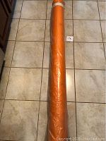 Full length view of orange-wrapped fabric cloth roll on tiled floor, showing approximate scale and size.