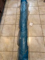 Full length view of blue fabric roll wrapped in plastic, lying on tiled floor.