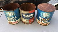 Three vintage metal cans with White Rose and Prestone anti-freeze branding showing rust and missing tops or bottoms.