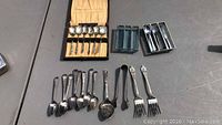 Photo showing various sterling spoons, forks, and sugar tongs laid out on a surface, including Apostle spoons still in the fitted lined case.