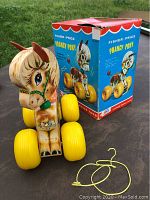 Fisher Price Prancing Pony wooden pull toy with large yellow wheels sitting in front of original box outdoors on table, photo shows pony head and body details.