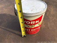 Front view of the York Peanut Butter tin beside a tape measure showing height of approximately 6 inches.