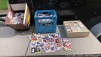 View of hockey cards spread on table, blue crate filled with cards, and a cardboard box of cards beside them