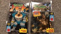 Three Spawn action figures in original packaging, two showing the blue and white Inferno figure and one showing the golden armored warrior figure.