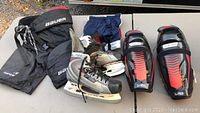 Bauer junior hockey pants, navy shorts, silver size 6 skates, red and black shin pads on table.