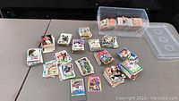 Table with multiple stacks and a plastic container of assorted football trading cards spread out.