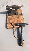 Full view of mini anvil set including anvil on wood block and hammer with leather strap.