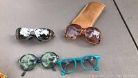 All four pairs of glasses arranged on a table showing styles and colors, brown leather case placed next to amber sunglasses