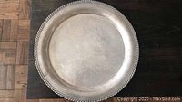 Top view of a large round silver tray with decorative rope border and plain surface showing wear