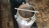 Copper milk can with lid showing top and horizontal securing bar.