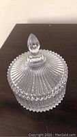 Closed glass dish with lid showing ribbed, scalloped design and finial handle.