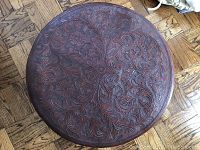 Top view showing detailed carved floral and vine pattern on the leather surface of the ottoman.