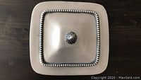 Top view of square pewter lid with beaded border and knob handle.