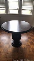 Round solid mahogany pedestal table in front of windows