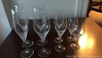 Collection of eight etched stemware glasses including champagne, wine, shot, cordial, and liqueur glasses arranged on wooden table