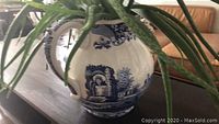Blue and white ceramic planter partially filled with aloe succulent plant, showing the side handle and detailed scenic motifs.