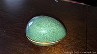 Front view of one speckled green porcelain egg with gold trim on a dark wooden surface.