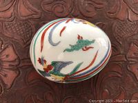 Close-up of first porcelain accent egg with vibrant bird and cloud design on glossy finish.
