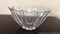 Clear crystal vase shaped like a flower with petal scalloped edges, photographed from the side on a dark surface.
