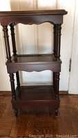 Front view of mahogany 3-tier shelf showing three levels with scalloped trim and turned legs.