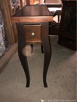 Front and right side view showing single drawer with round metal knob and curved cabriole legs.