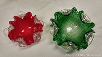Top view of two Murano glass bowls, one red and one green, showing wavy ruffled edges and clear bubble accents.