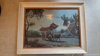 Framed watercolor painting showing a village scene with an ox-cart and huts, signed A.B. Ibrahim.