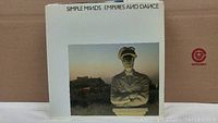 Simple Minds Empires and Dance vinyl record album cover featuring a statue in front of a hill at sunset, white border, and title text on top.